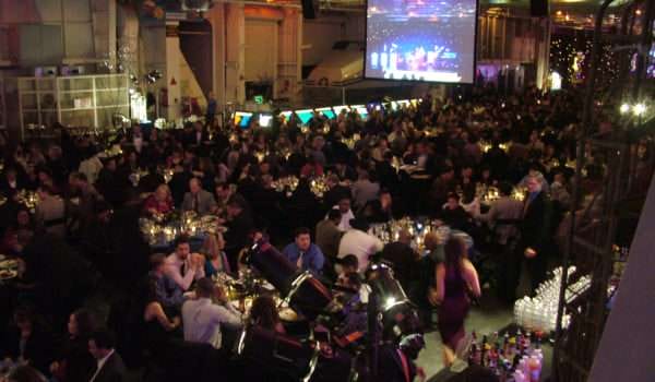 Large crowd seated at gala dinner with projected presentation on screen.